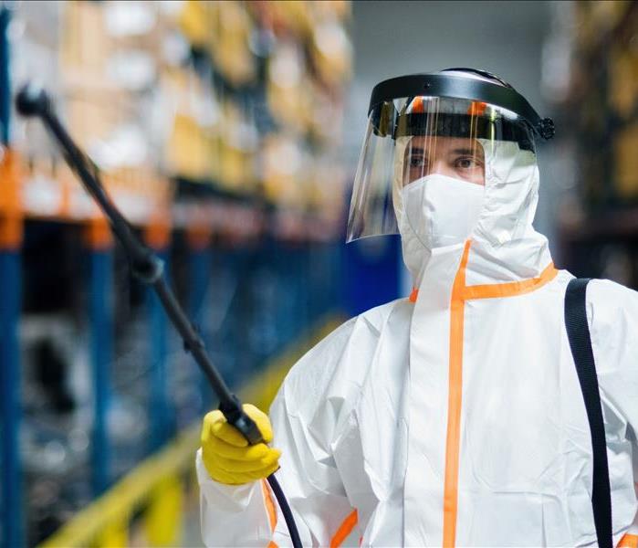 Male worker with protective mask and suit disinfecting industrial factory with spray gun